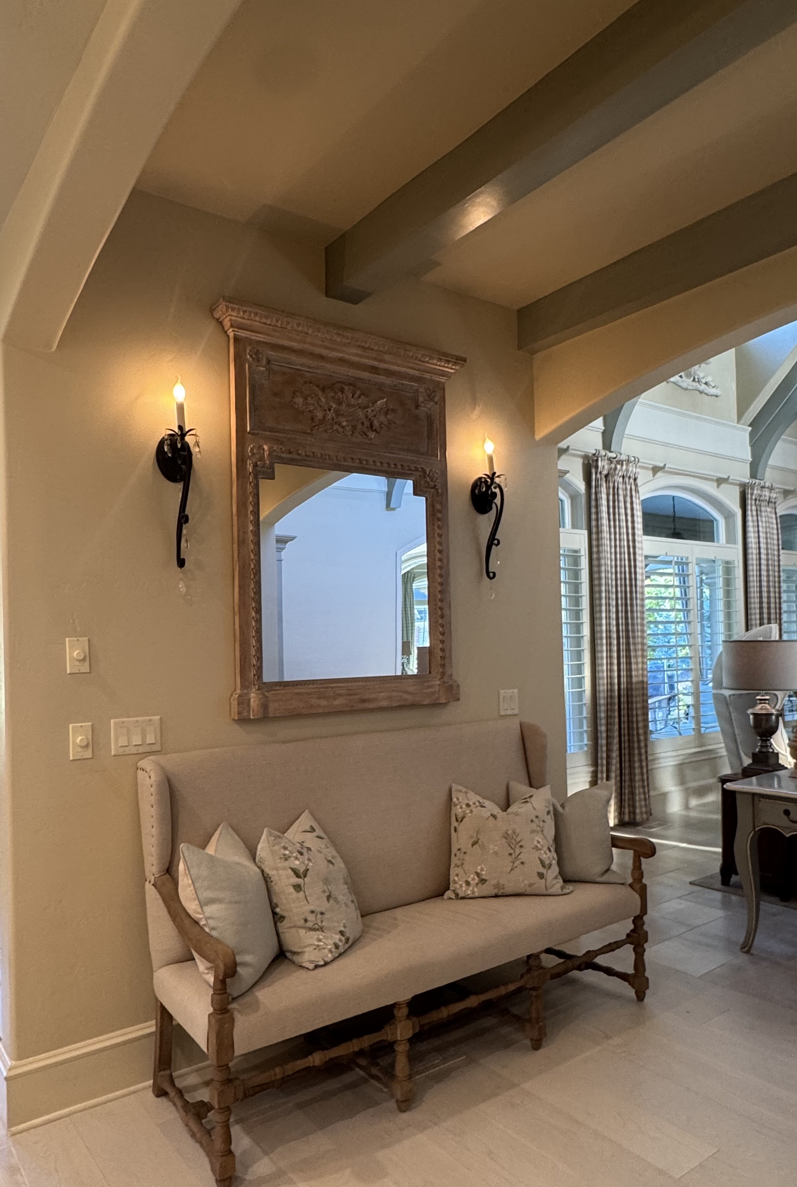 An upholstered bench beneath a carved wood mirror and candle-style sconces.