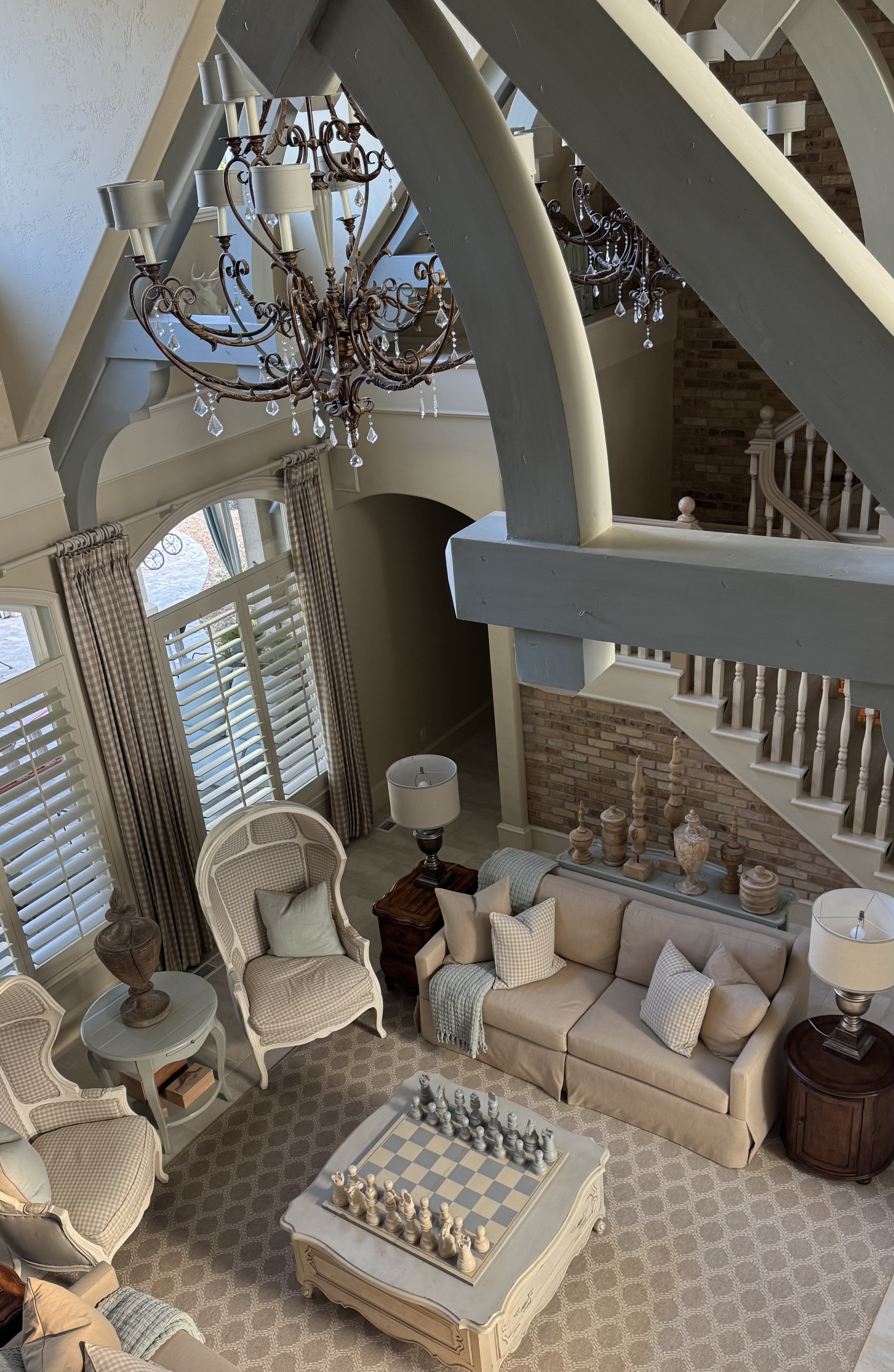 A Country French living room with curved beams, chandeliers, checked chairs, and a soft blue palette.