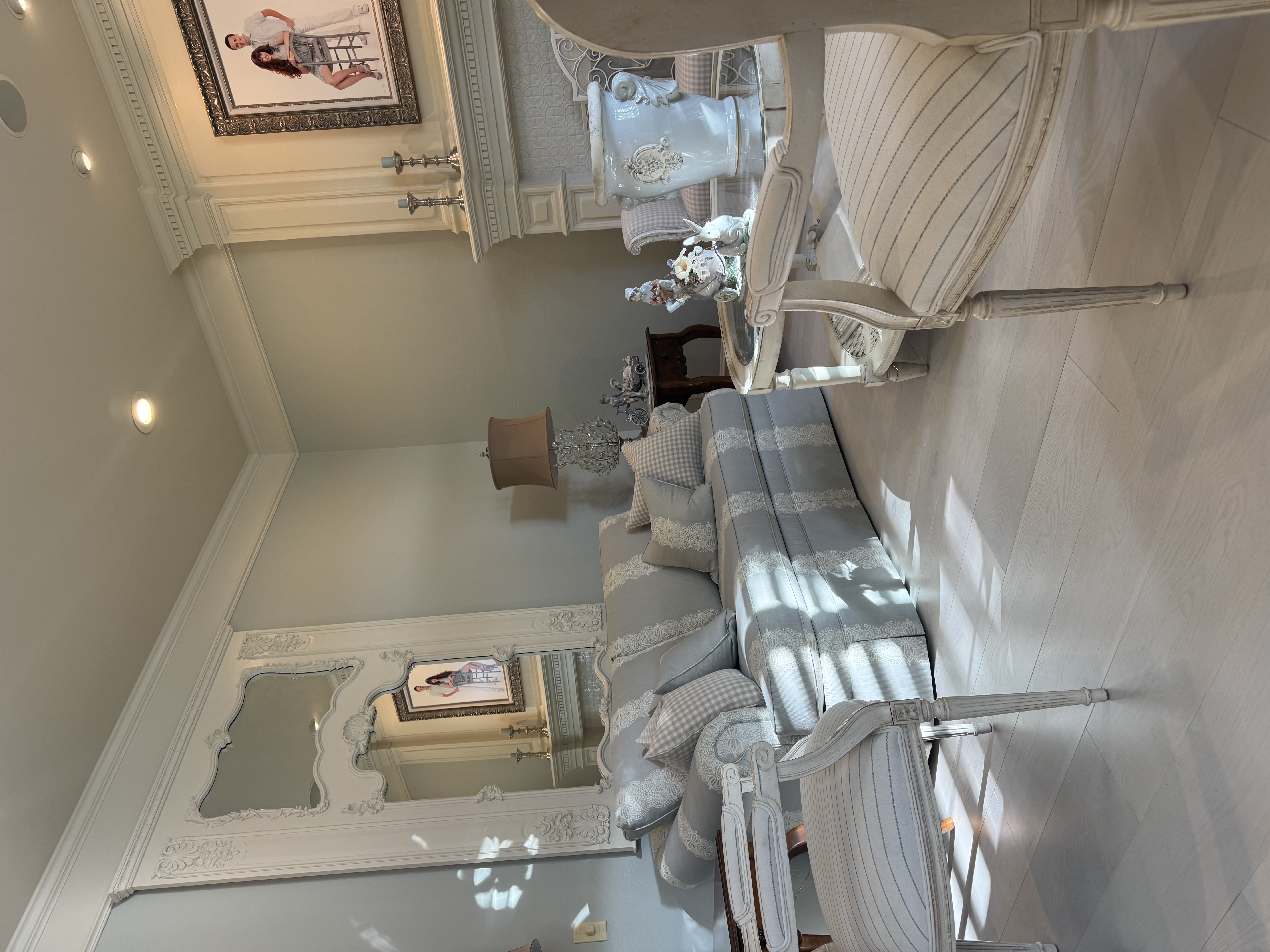 A pale blue sitting room with carved cream chairs, patterned upholstery, and an ornate mirror.